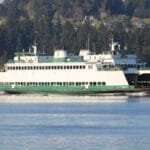 A Washington State Ferry sailing on the calm waters near Port Orchard, with a forested landscape in the background.