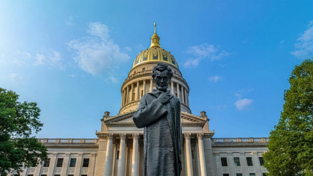 Facade of the West Virginia State Capitol building with a statue of Abraham Lincoln in the foreground under clear blue skies.