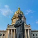 Facade of the West Virginia State Capitol building with a statue of Abraham Lincoln in the foreground under clear blue skies.