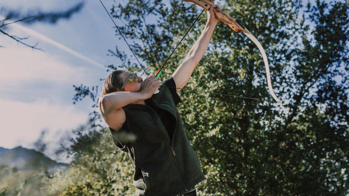 Woman practicing archery outdoors with a bow at a shooting range.