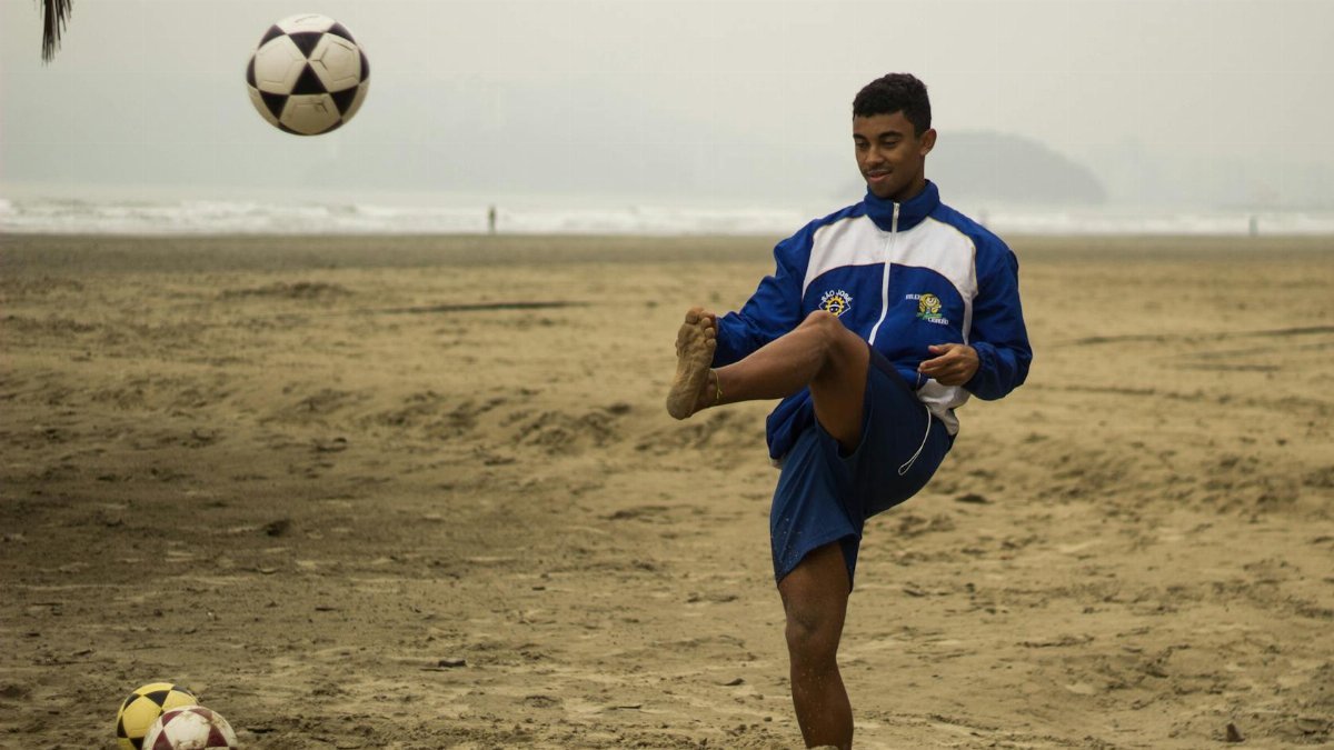 A young male athlete practices soccer on a sandy beach, showcasing skill under cloudy skies.