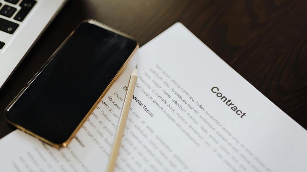 Close-up of a contract document alongside a smartphone and laptop, ideal for business concepts.
