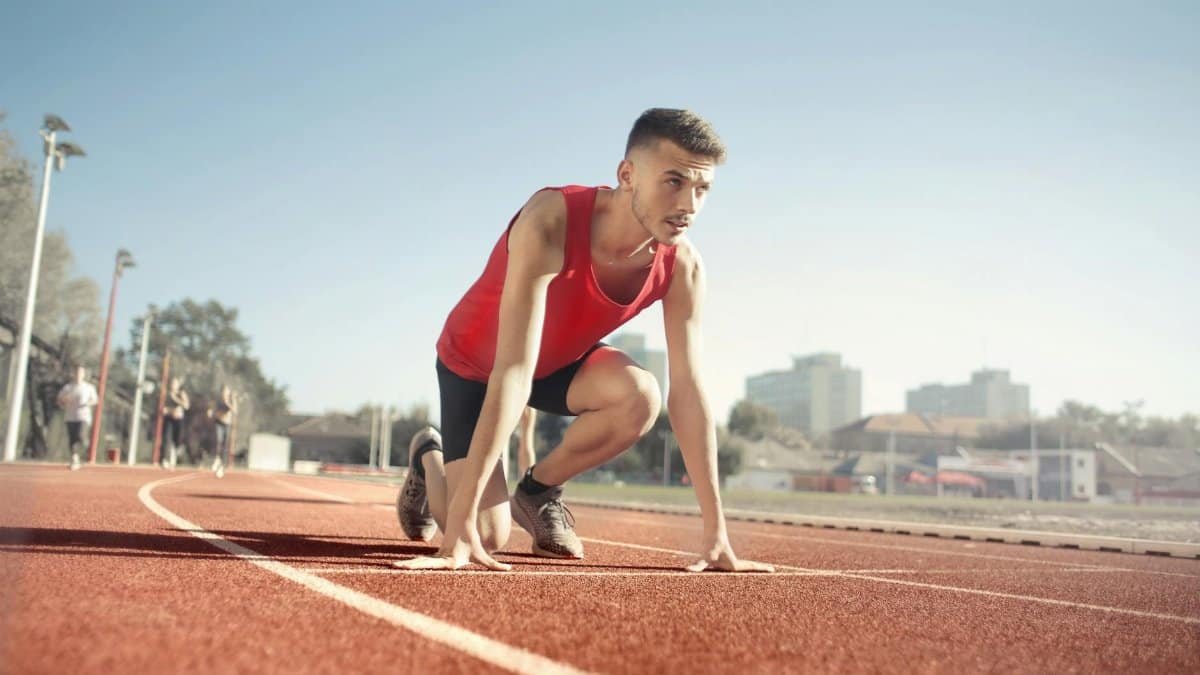 Young male athlete in start position on outdoor track, ready to sprint.