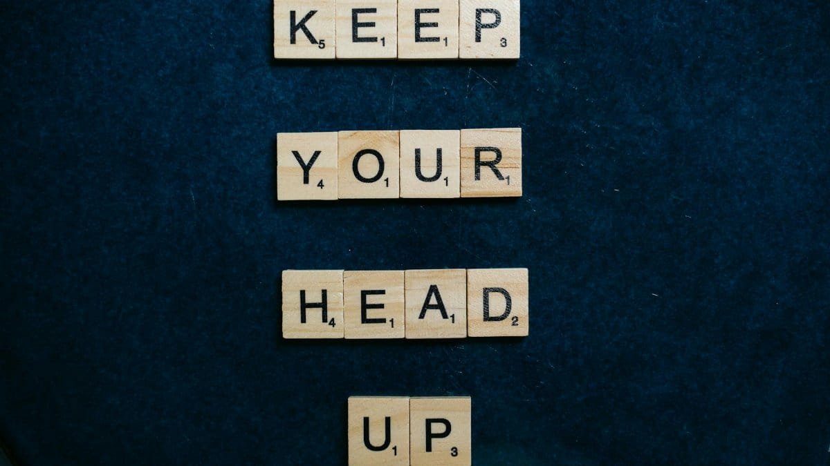 Inspirational message 'Keep Your Head Up' in Scrabble tiles on a dark blue background.