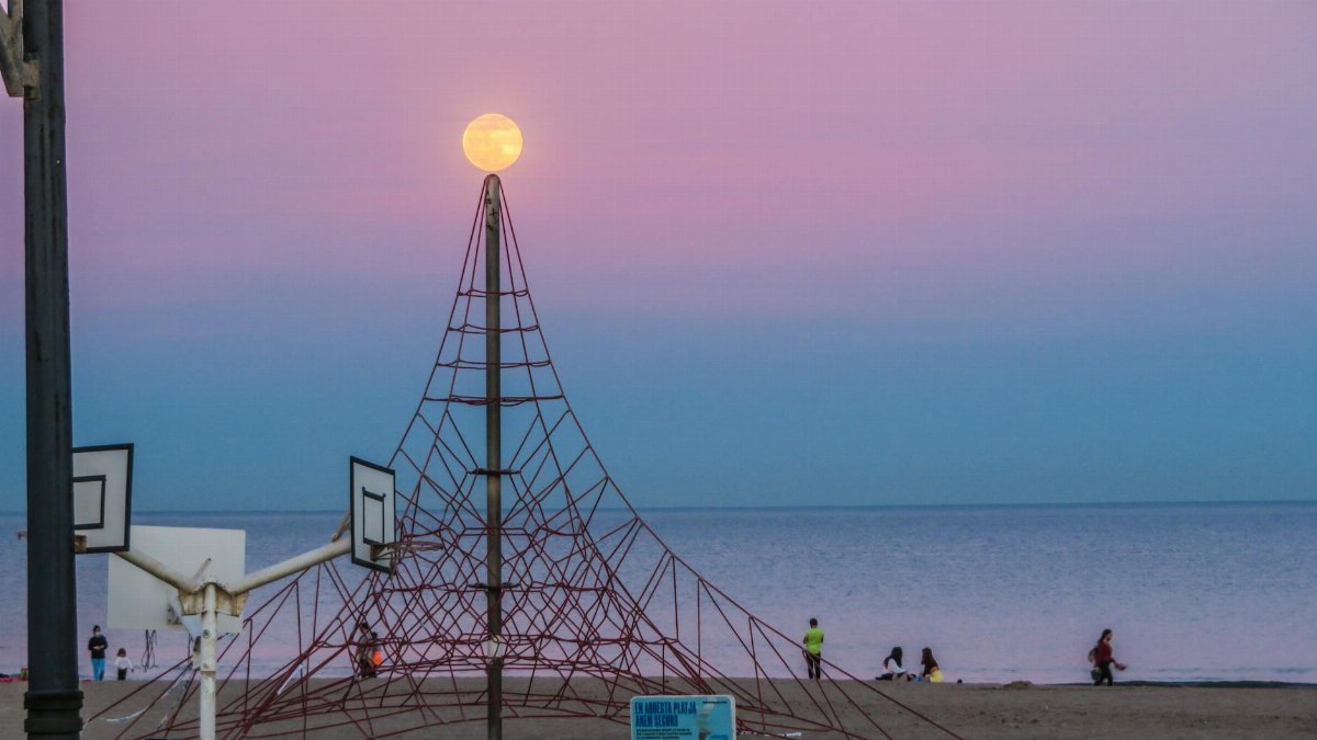 Pink twilight sky over seaside playground with moon setting over a climbing structure.