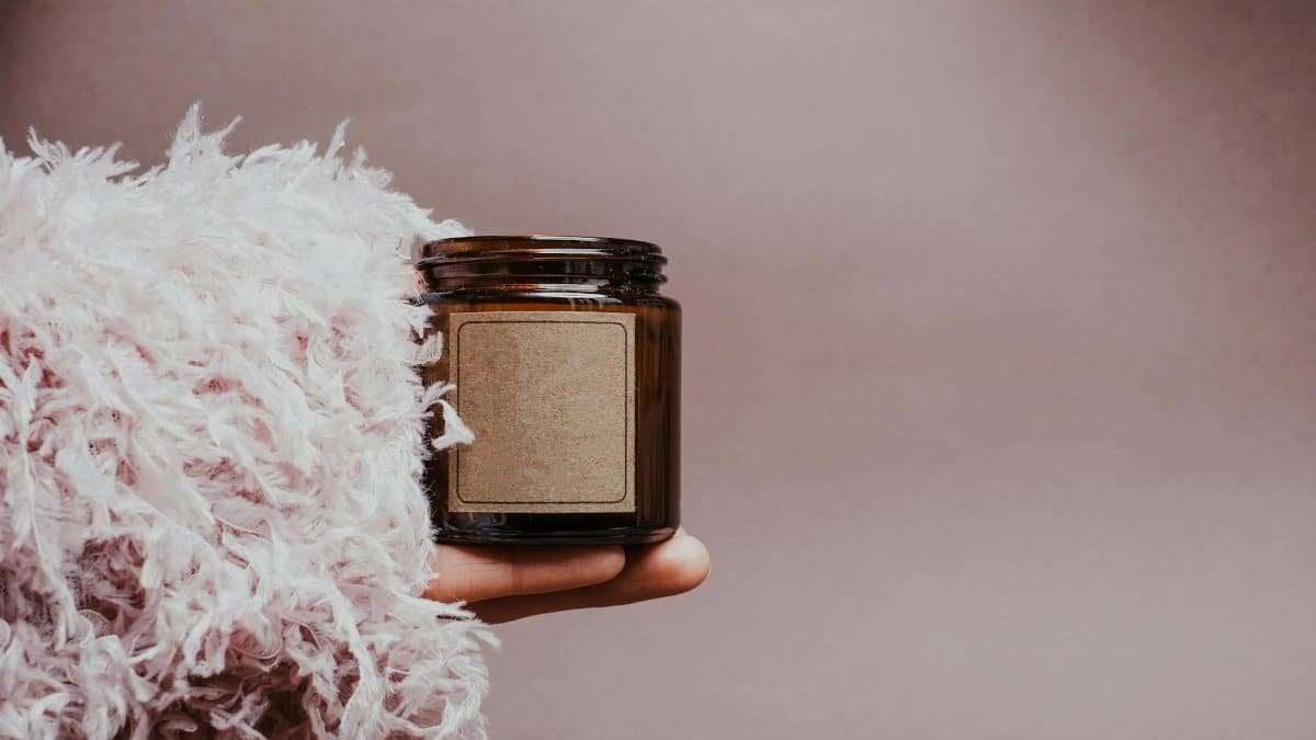 A brown glass jar held by a feather-covered hand on a gray background, showcasing eco-friendly design.
