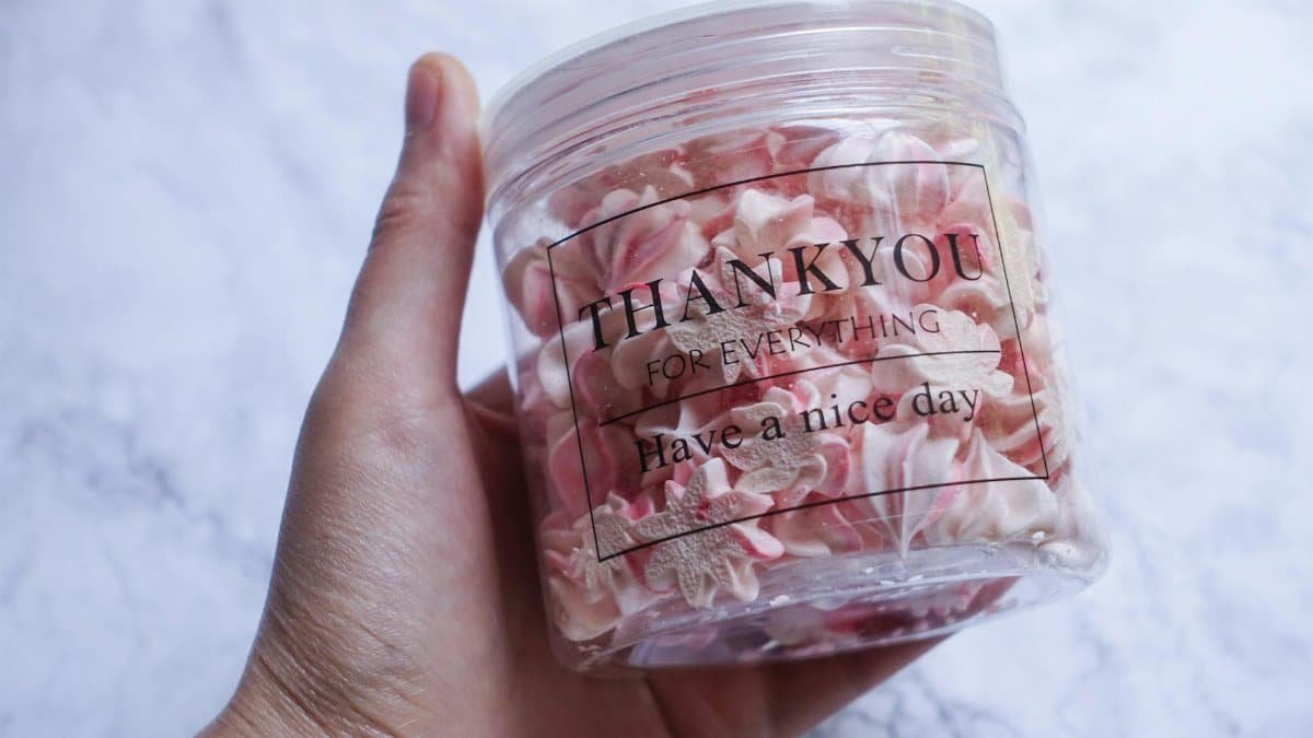 Close-up of a hand holding a jar of pink meringue cookies with a 'Thank you' message.