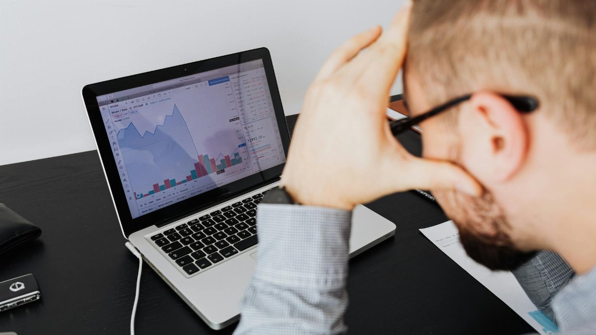 Over the shoulder view of a man analyzing financial data on a laptop screen.