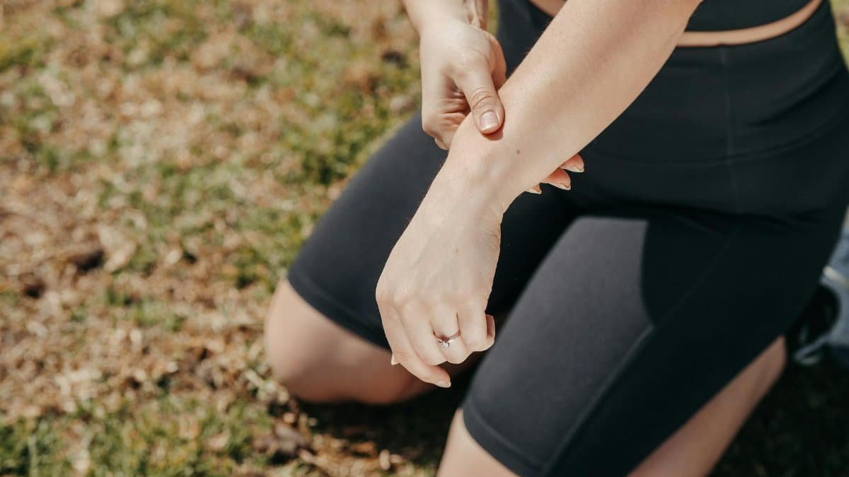 Close-up of a person kneeling outdoors while checking their arm in active wear.