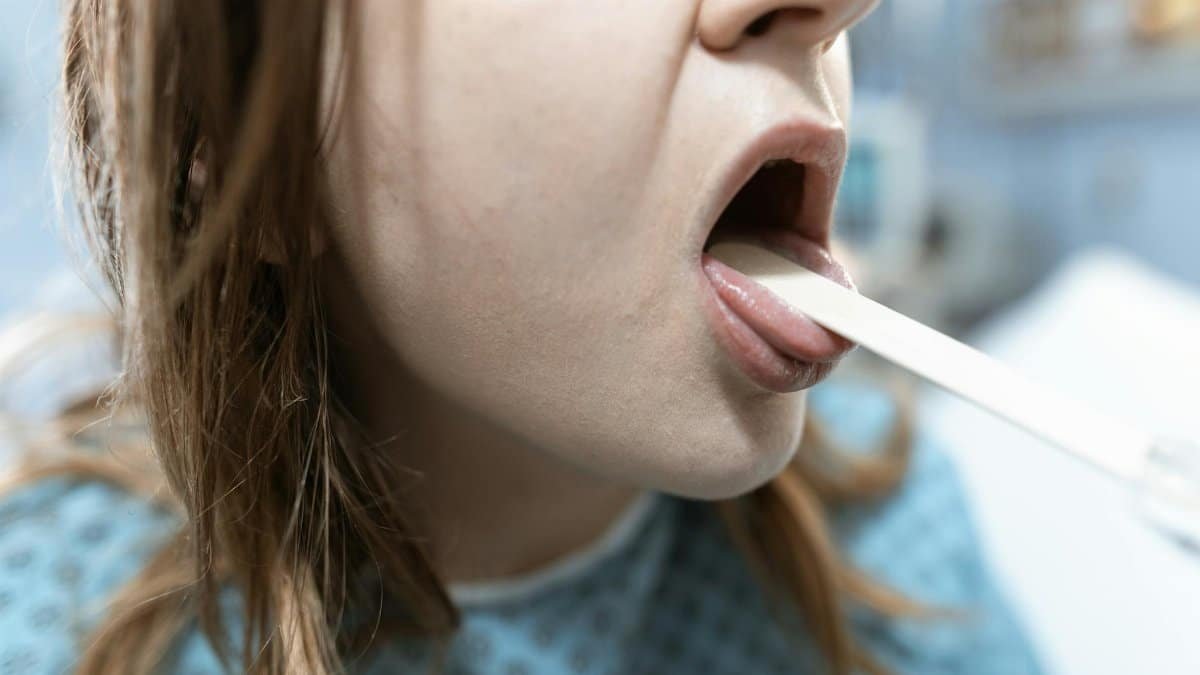 Close-up of a woman having her throat examined in a medical setting with a tongue depressor.