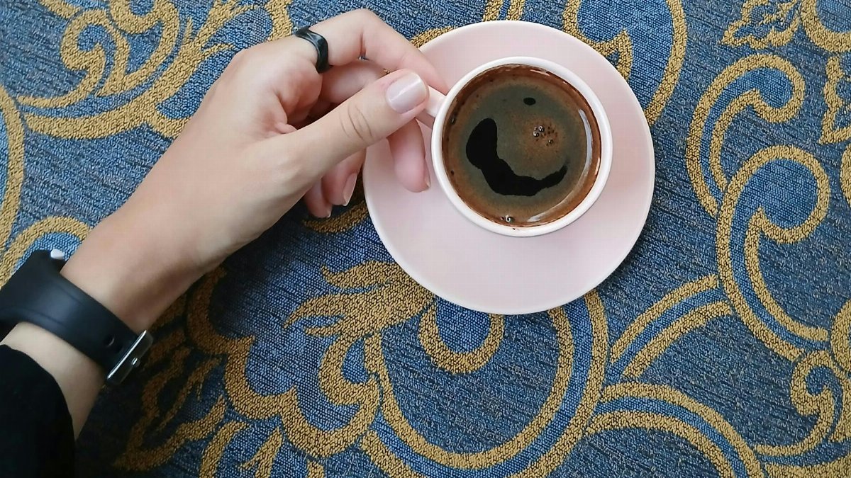 Top view of a person holding an espresso cup on a luxurious patterned carpet.