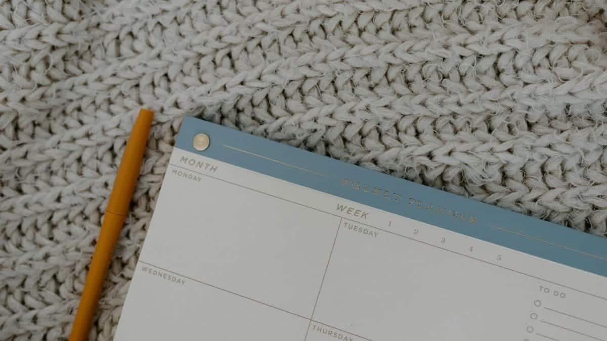 Weekly planner and pen on knitted fabric, perfect for organizing plans.