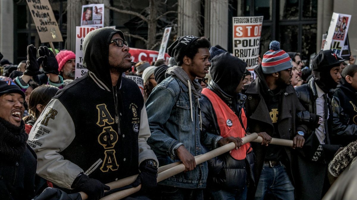 Protesters march in New York City against police brutality, holding signs and banners.