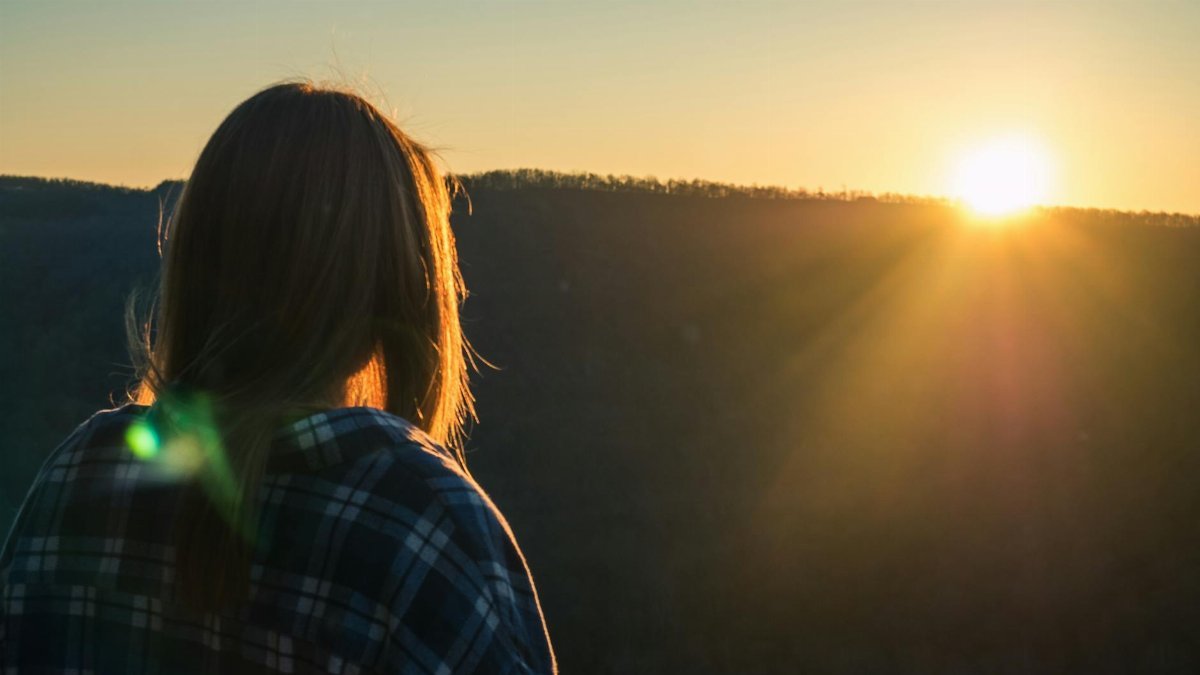 A woman views a beautiful sunset over hills in Fayetteville, Arkansas, showcasing nature's serene beauty.