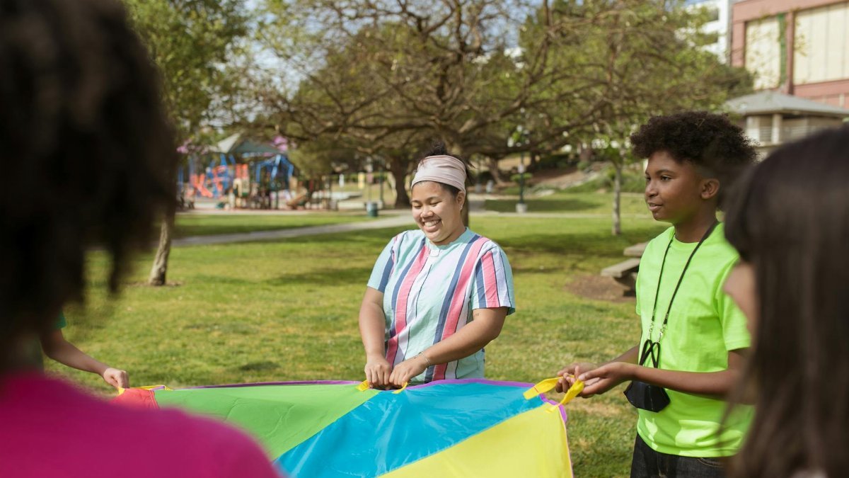 Happy kids enjoying outdoor activities with a colorful parachute at a summer camp.