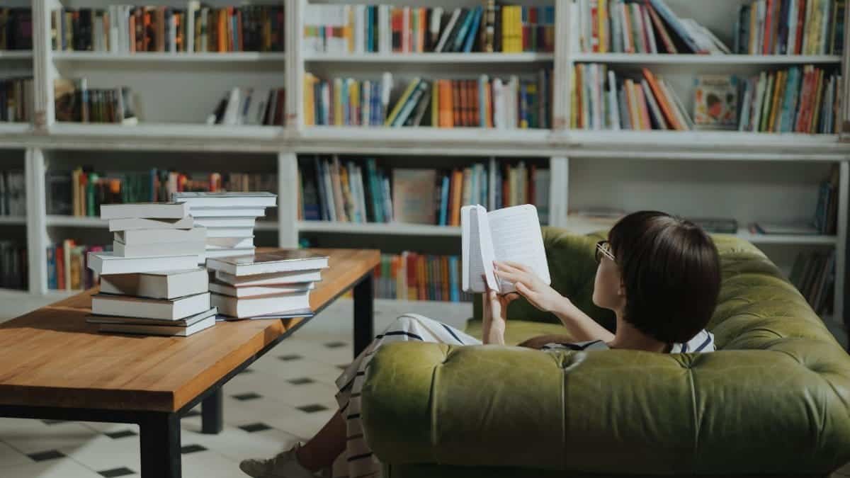 Woman reading on a sofa in a cozy library surrounded by book stacks.
