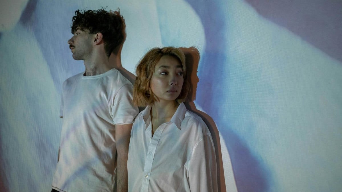 An interracial couple standing apart in an artistic shadow setting, depicting tension and emotional distance.