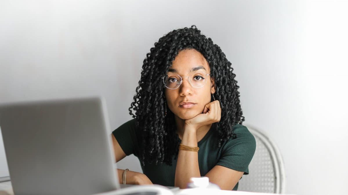 Young woman with glasses working attentively on a laptop at a bright desk.