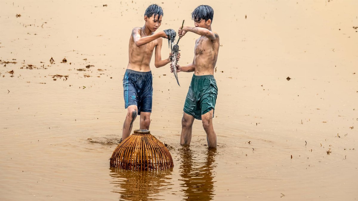 Two teenagers fishing in a rural wetland, showcasing traditional methods and summer recreation.