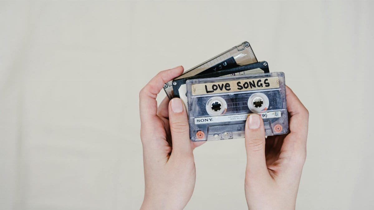 Close-up of hands holding retro cassette tapes labeled 'Love Songs' on a light background.