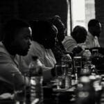 A diverse group of adults engaged in a dinner meeting, captured in black and white.