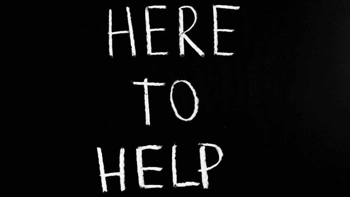 White text 'Here to Help' on a minimalist black chalkboard background, conveying encouragement and support.