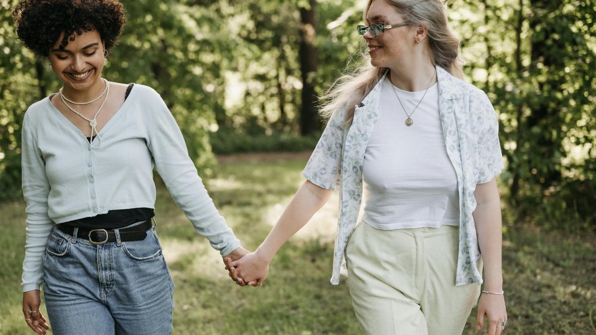 A loving couple holds hands while strolling through a lush, sunny park setting.