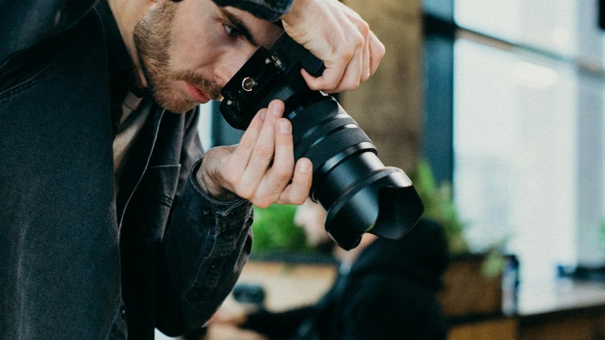 A male photographer capturing images indoors using a DSLR camera.