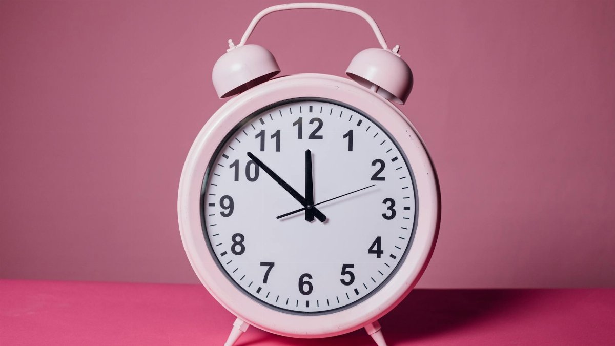 Pink retro alarm clock on a pastel pink background symbolizing time and punctuality.