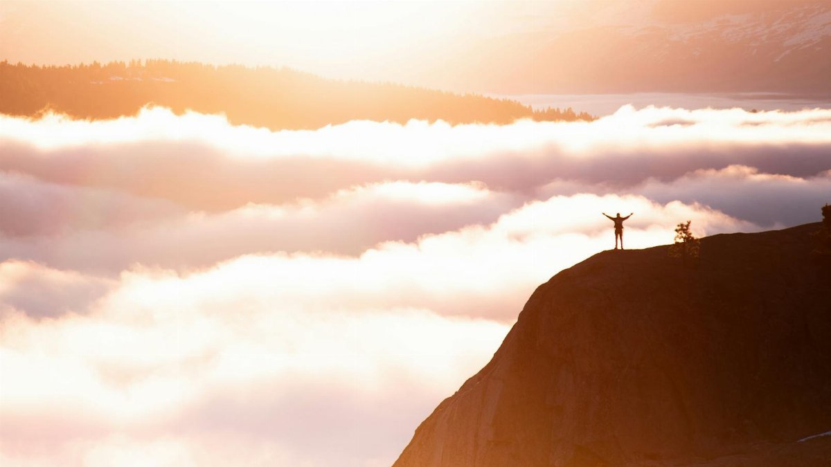 Silhouette of a person standing triumphant on a mountain cliff amidst the breathtaking morning clouds.