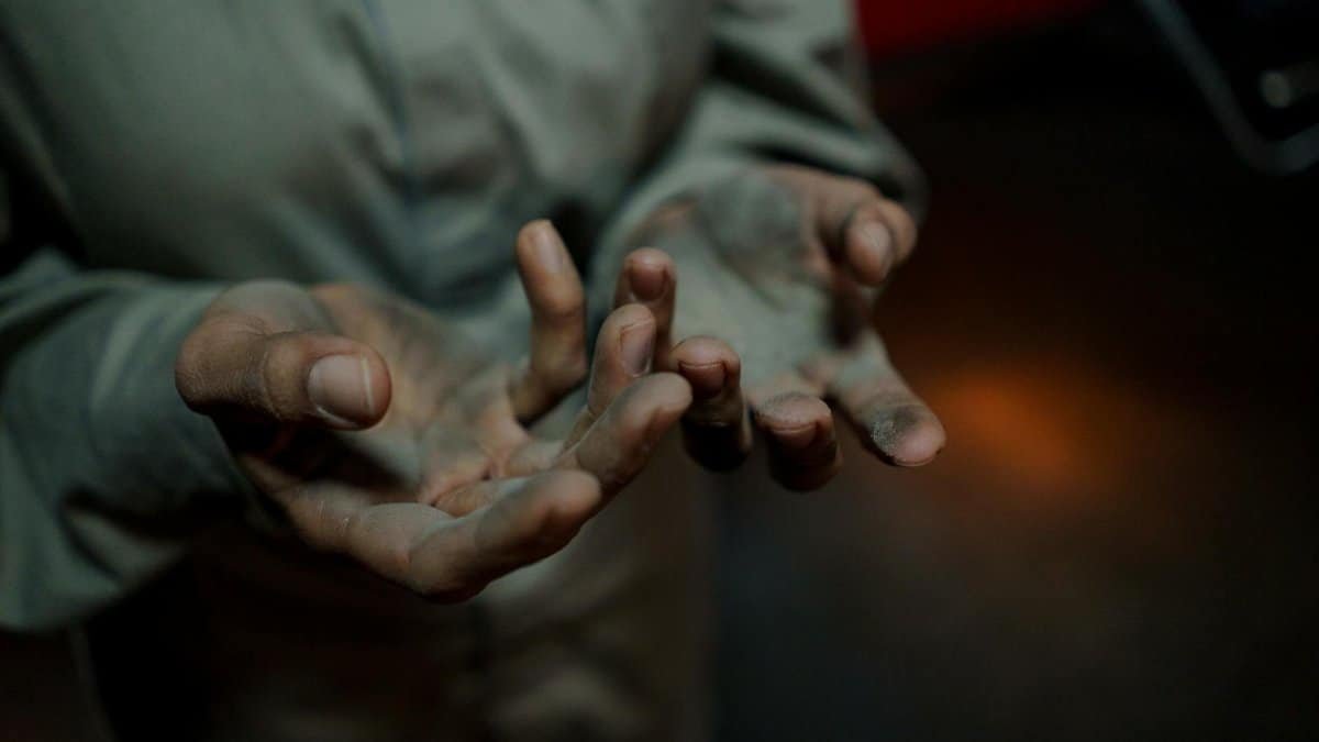 A close-up showing dirty hands of an adult worker wearing gray long sleeves, conveying hard work.
