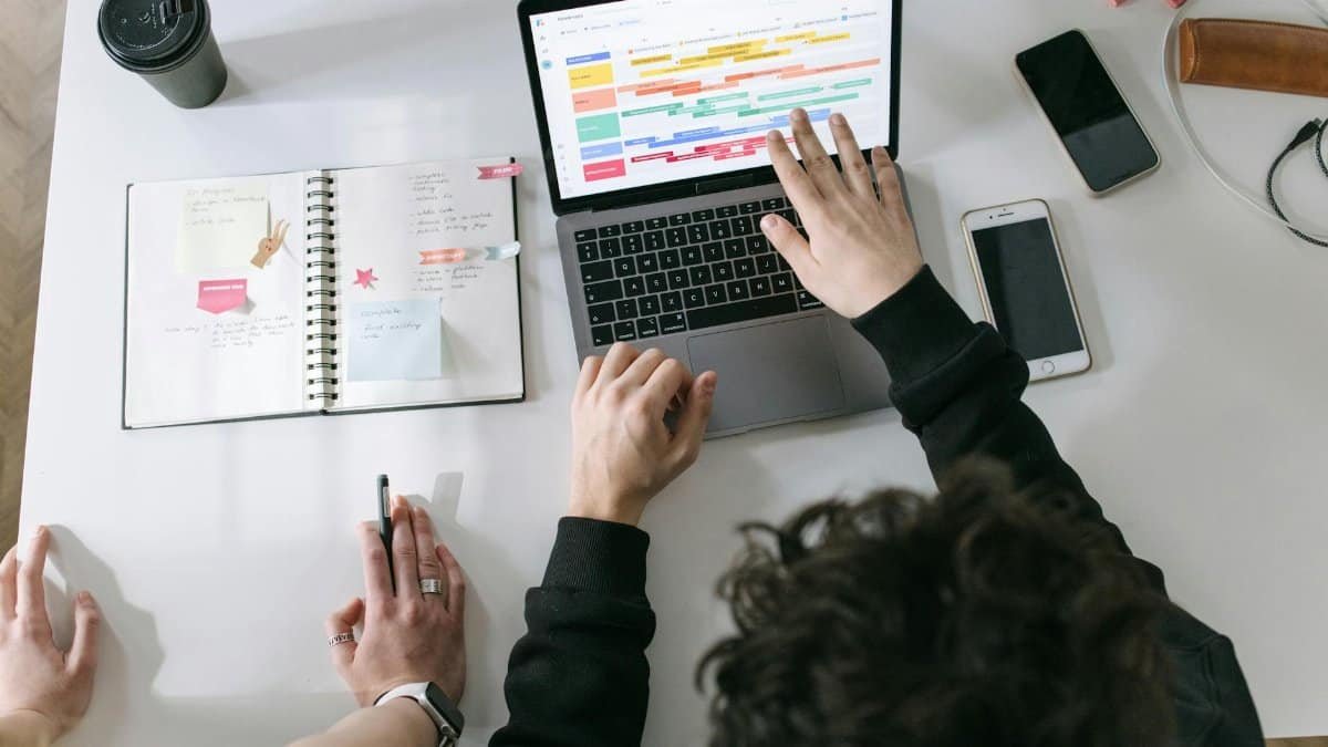 Two people collaborating on a laptop and planner at a vibrant modern office desk.