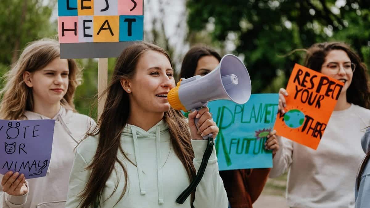 Group of young women passionately protesting for environmental change with signs and a megaphone.