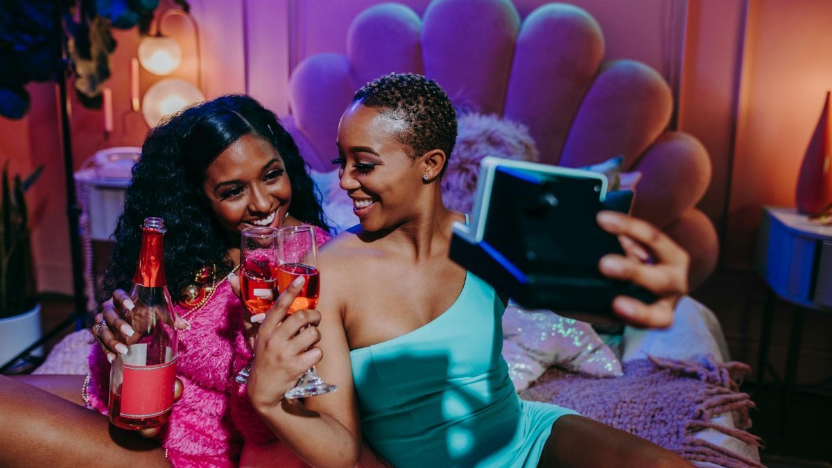 Two women joyfully enjoying a holiday celebration, taking selfies and enjoying drinks indoors.