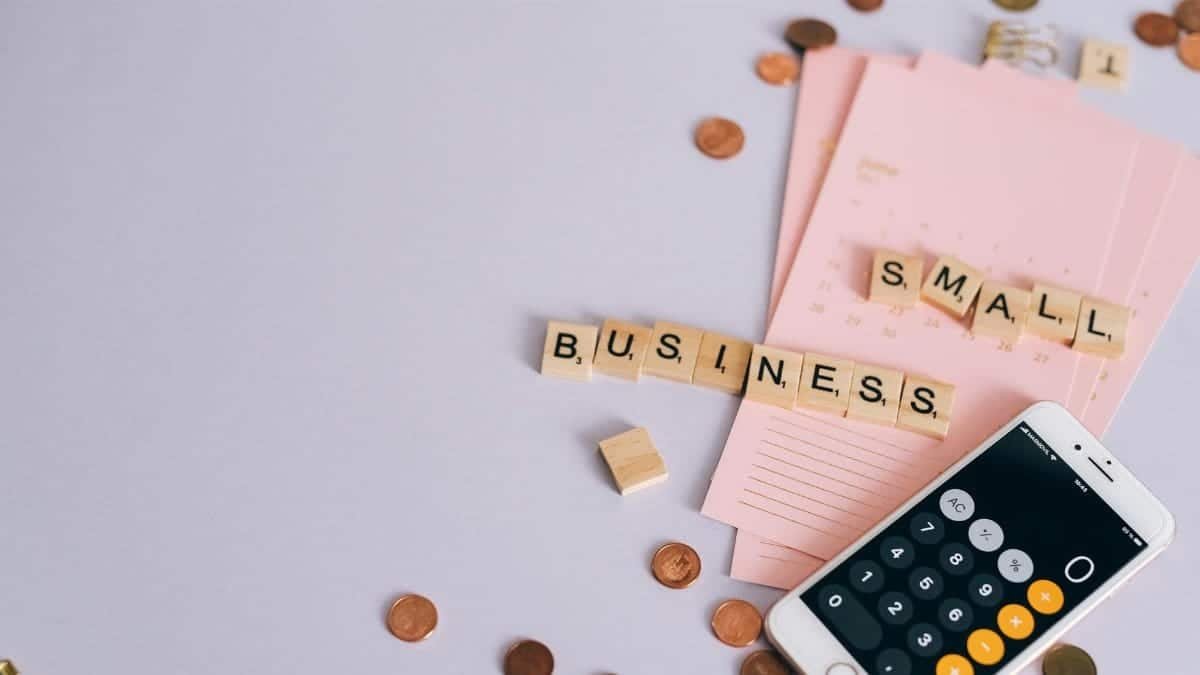 Flat lay of a small business planning scene with coins, smartphone calculator, and letter tiles.