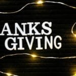 Festive Thanksgiving message illuminated by warm string lights on a dark background.