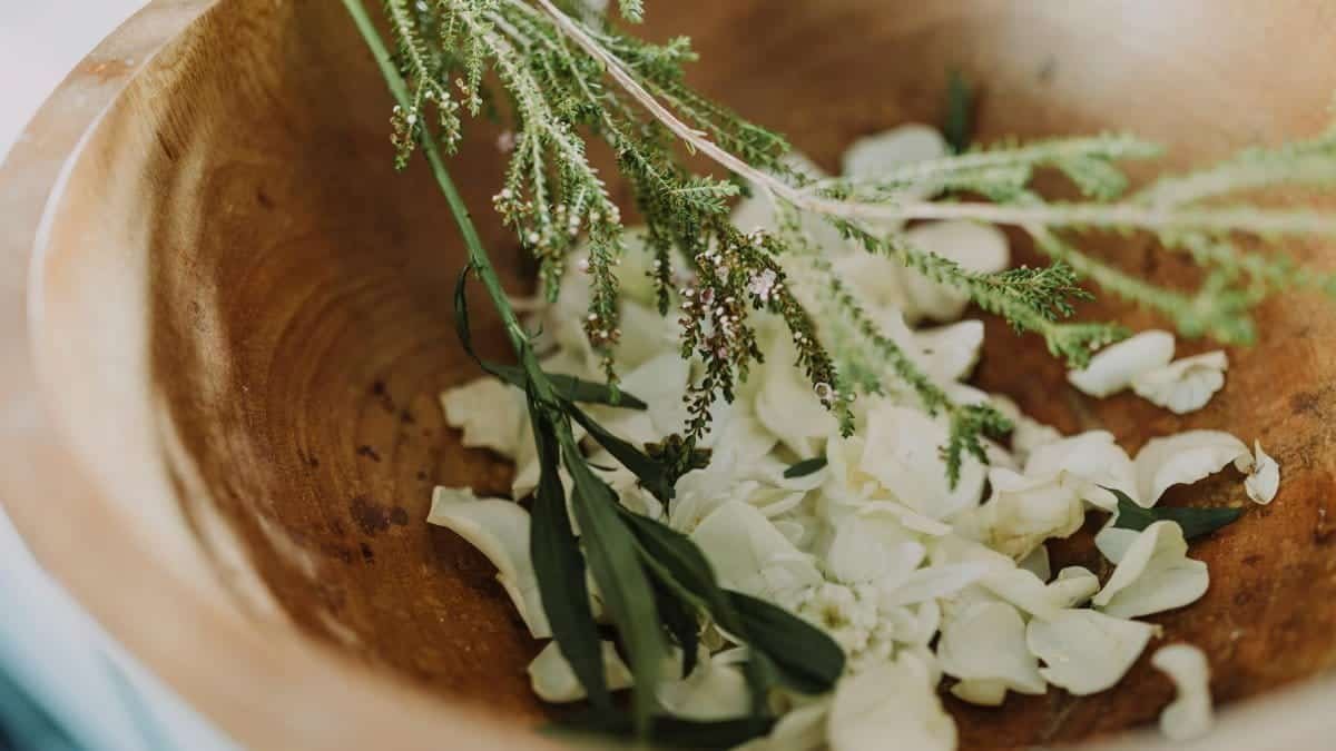 Wooden bowl filled with fresh herbs and flowers for aromatherapy and relaxation.