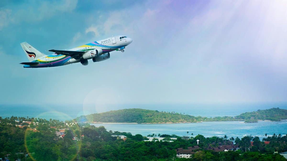 Airplane soaring over Koh Samui island, Thailand, showcasing a vibrant tropical landscape in daylight.