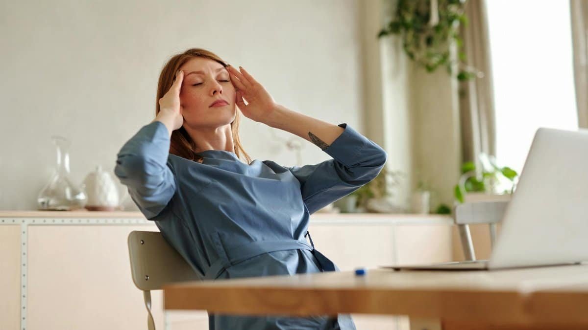 Woman experiencing stress at work, sitting at desk with a laptop, indoors.