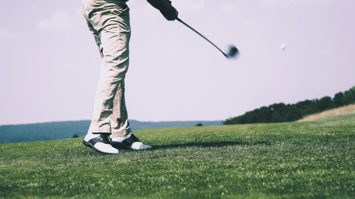 A golfer in mid-swing on a sunny day at the golf course, showing motion and focus.