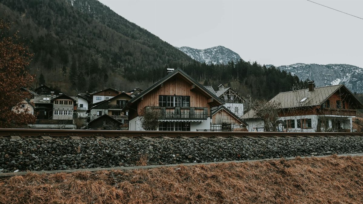 A serene winter landscape of a mountain village with wooden houses and a railway in the foreground.