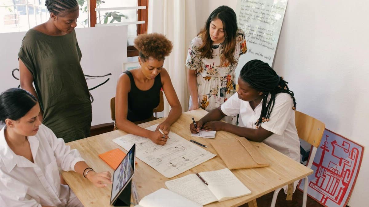 Diverse team collaborates on a project using digital and paper resources in a bright office.