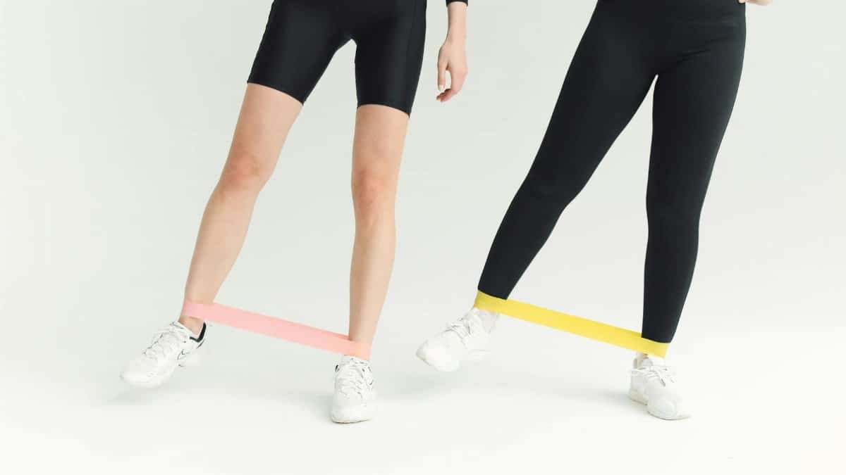 Two women exercising with resistance bands, focusing on leg workouts in a minimalistic setting.
