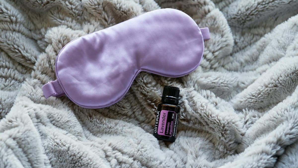 Lavender essential oil alongside a purple sleep mask on a gray blanket promotes relaxation and rest.