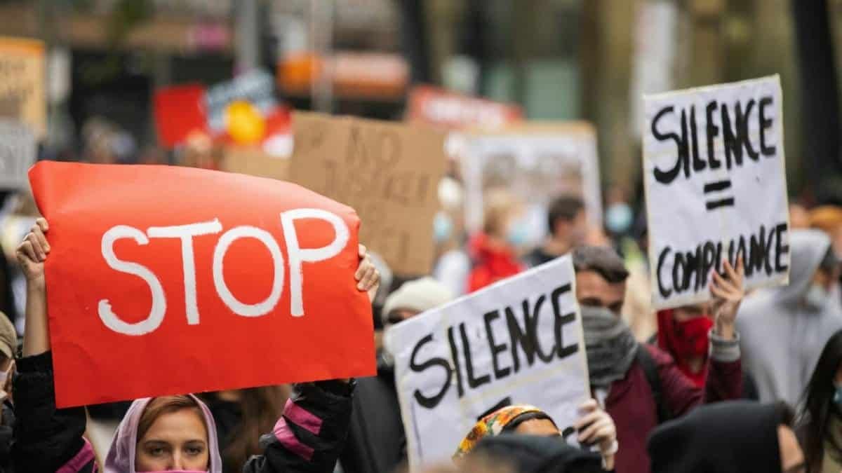 A diverse group of protesters hold signs reading 'STOP' and 'Silence = Compliance' during a rally in Melbourne.