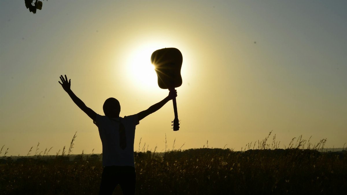 A young guitarist celebrates the sunrise with an acoustic guitar, creating a dramatic silhouette.
