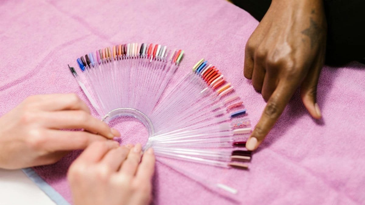 Hands selecting nail polish shades on color palette at salon. Manicure selection process.