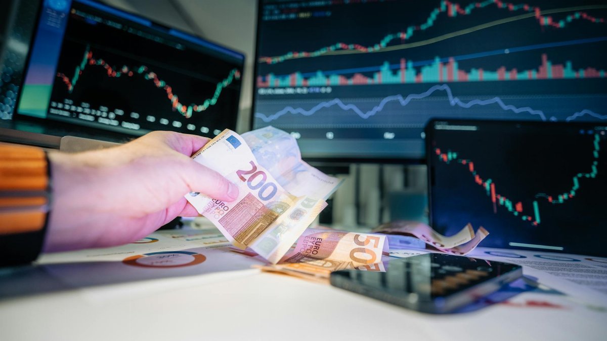 Close-up of euro banknotes with financial market graphs in the background, depicting finance and investment themes.
