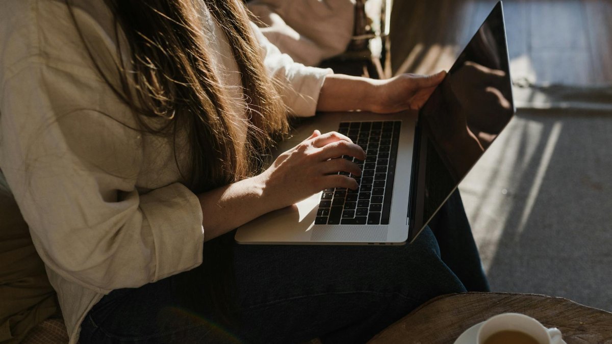Close-up of a woman using a laptop in a warm, cozy indoor setting with sunlight.