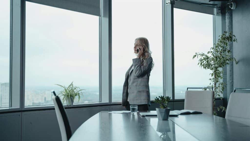 A professional woman makes a phone call in a sleek, modern office with city views.